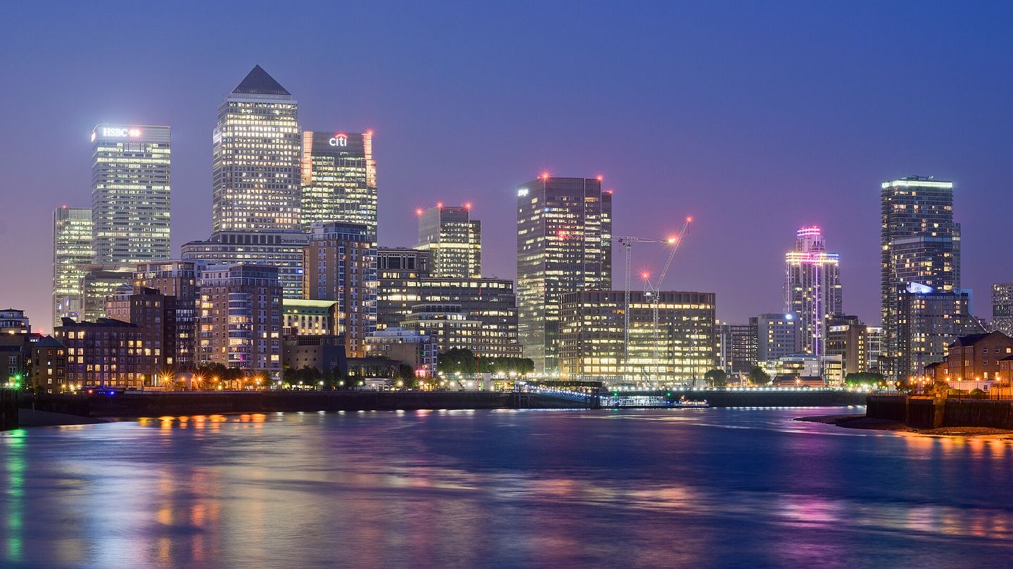 The lit office towers of Canary Wharf at night, seen across the Thames.
