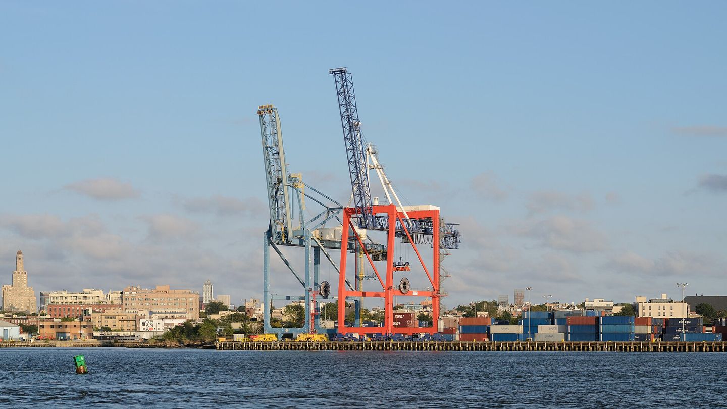 Gantry cranes and stacked containers at a working container terminal, seen across the water.