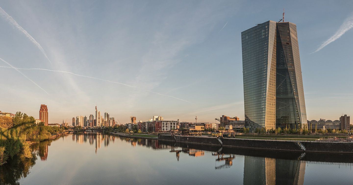 The European Central Bank tower and the Frankfurt skyline reflected in the Main at dawn.